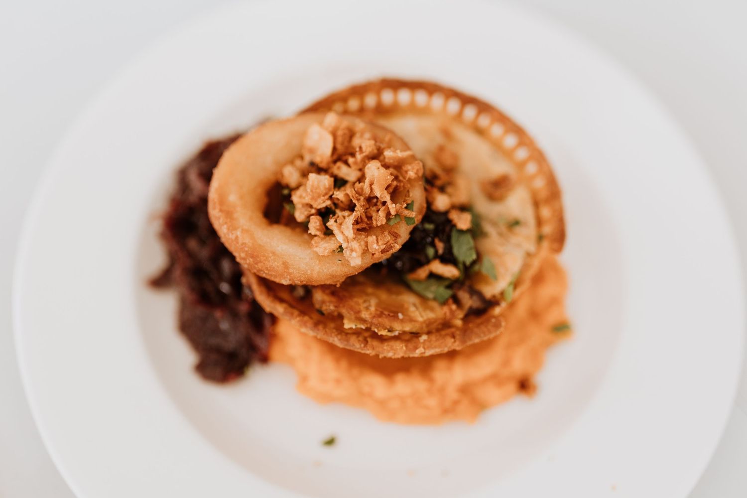 Gourmet pie stacked on a white plate topped with crispy onions and mash