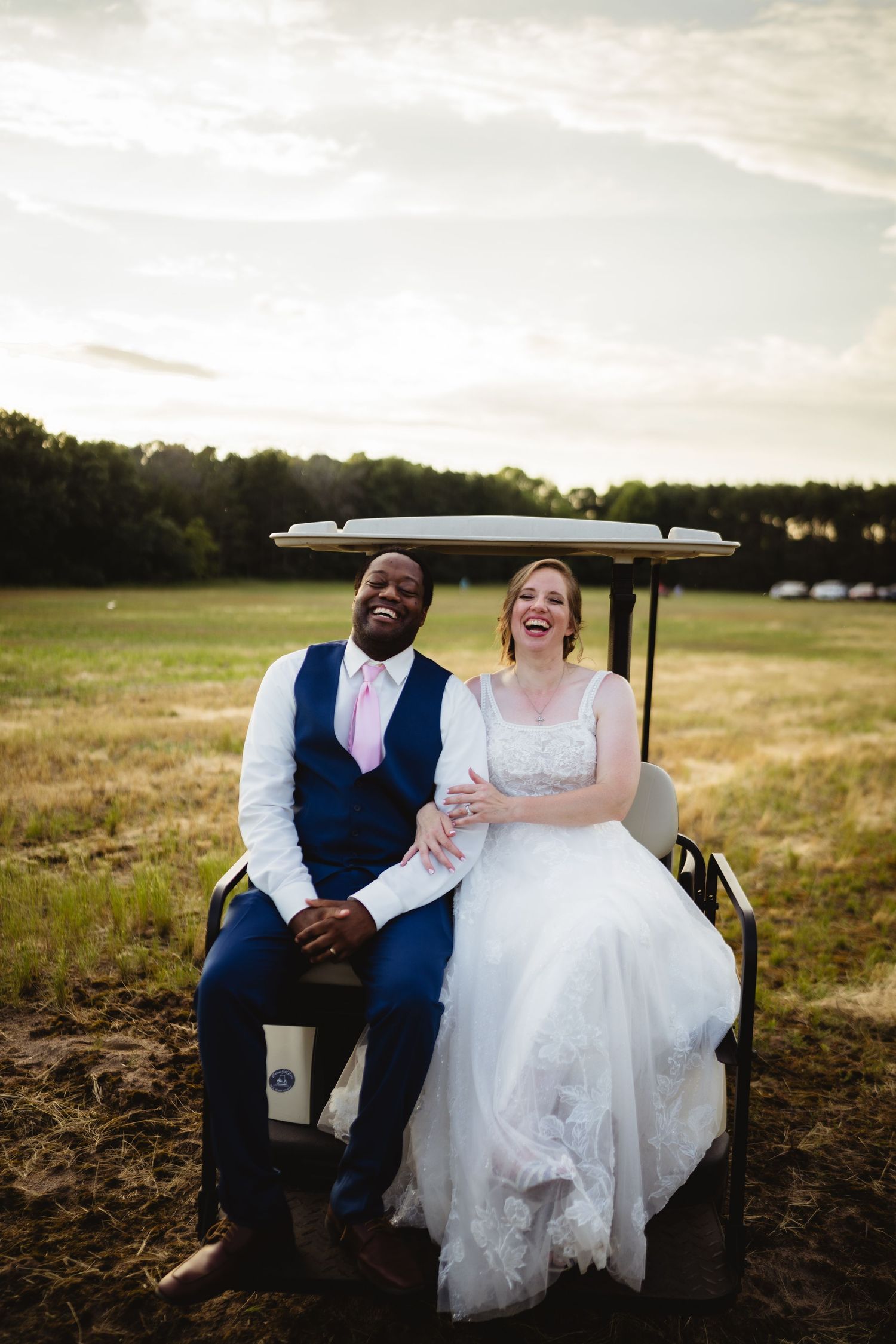 Loving couple shares joyful laughter while sitting together on a bench in a scenic field at sunset.