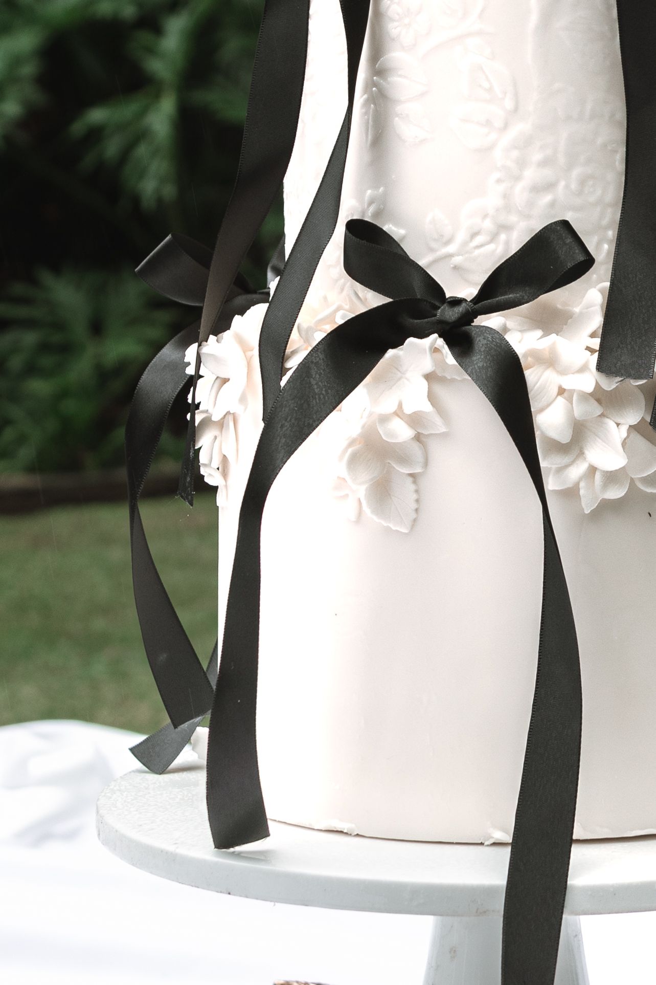 Close-up detail of an elegant white wedding cake decorated with black satin ribbons and delicate white sugar flowers.