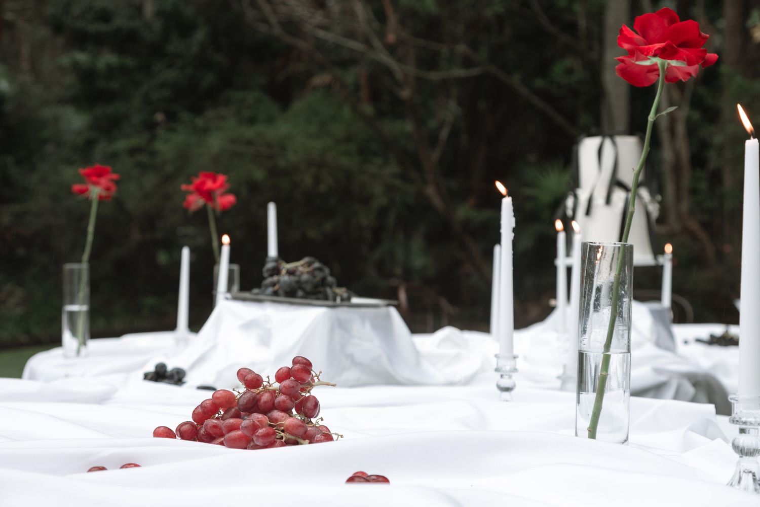 Elegant table setting with white linens, crystal glasses, and vibrant red flower centerpieces in a restaurant.
