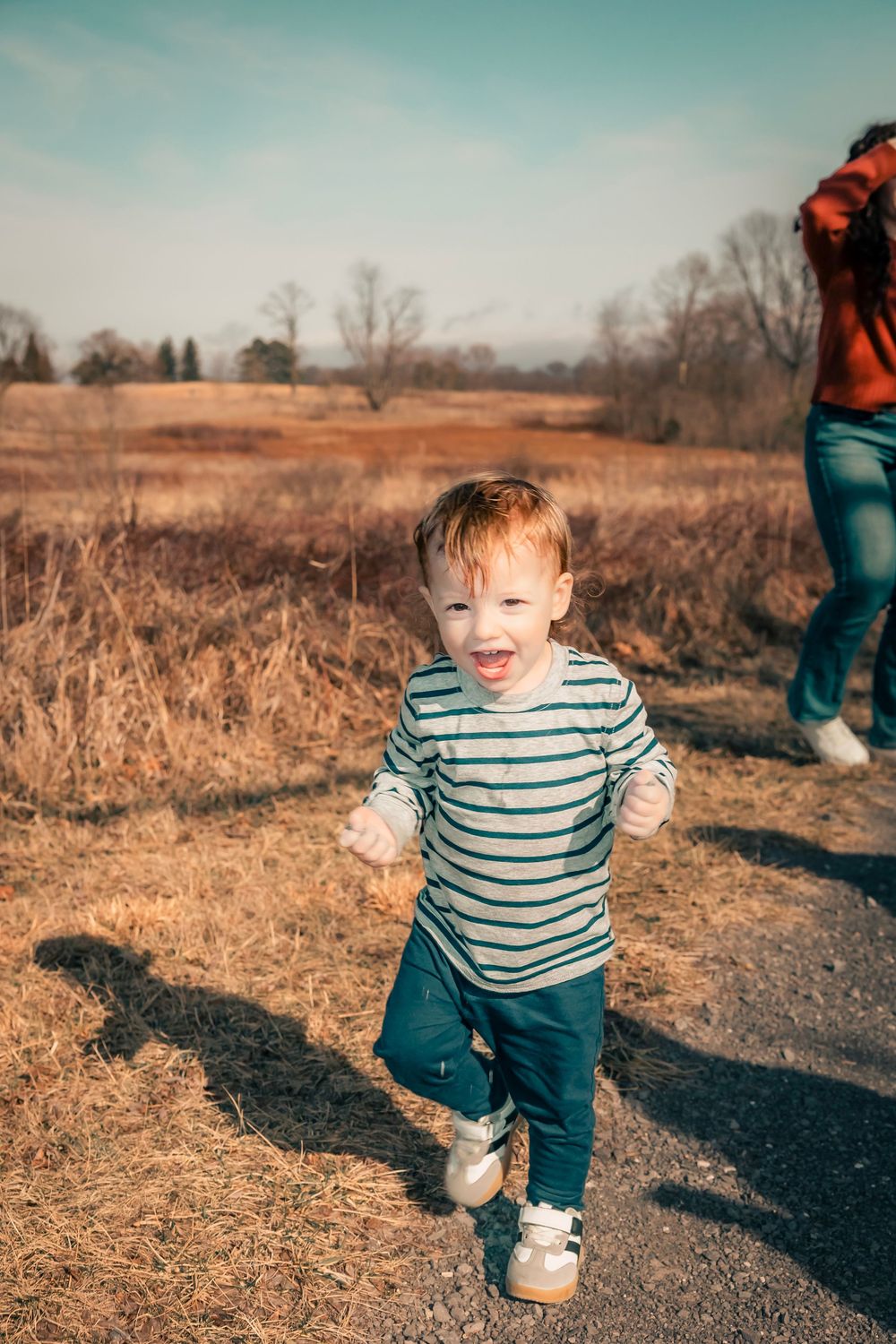 A toddler in a striped shirt explores a golden autumn field with tall grass during a sunny outdoor adventure.