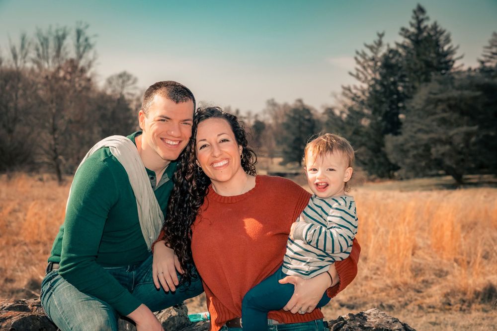 A family group wearing coordinated green and rust-colored outfits poses together outdoors in an autumn field.