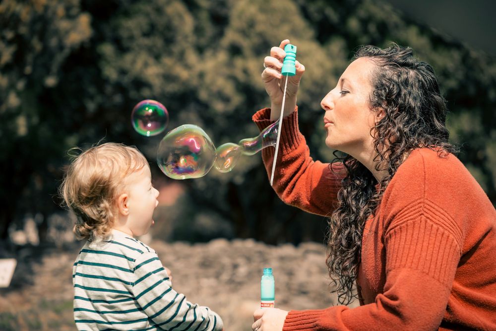 A child and adult play with soap bubbles outdoors on a sunny afternoon.