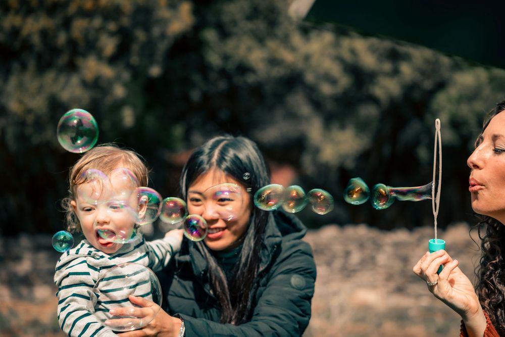 Two children play together outdoors while blowing bubbles on a sunny autumn day.