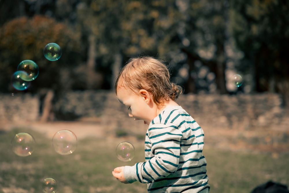 A small child in a striped shirt watches soap bubbles float by on a sunny autumn day.