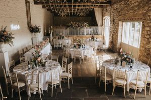 Rustic barn wedding reception venue with elegant white table settings and stone walls in natural light.