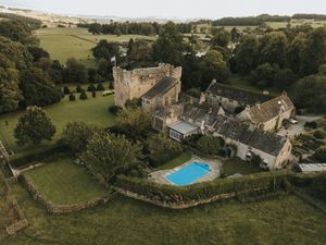 Aerial views showcase a rustic stone manor house with swimming pool nestled among rolling green countryside fields.