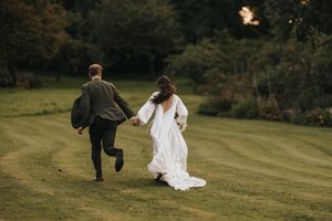 Couple walking hand in hand across a lush green hillside in elegant wedding attire.