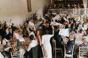 An energetic crowd of wedding guests celebrating and dancing during a reception in a rustic indoor venue.