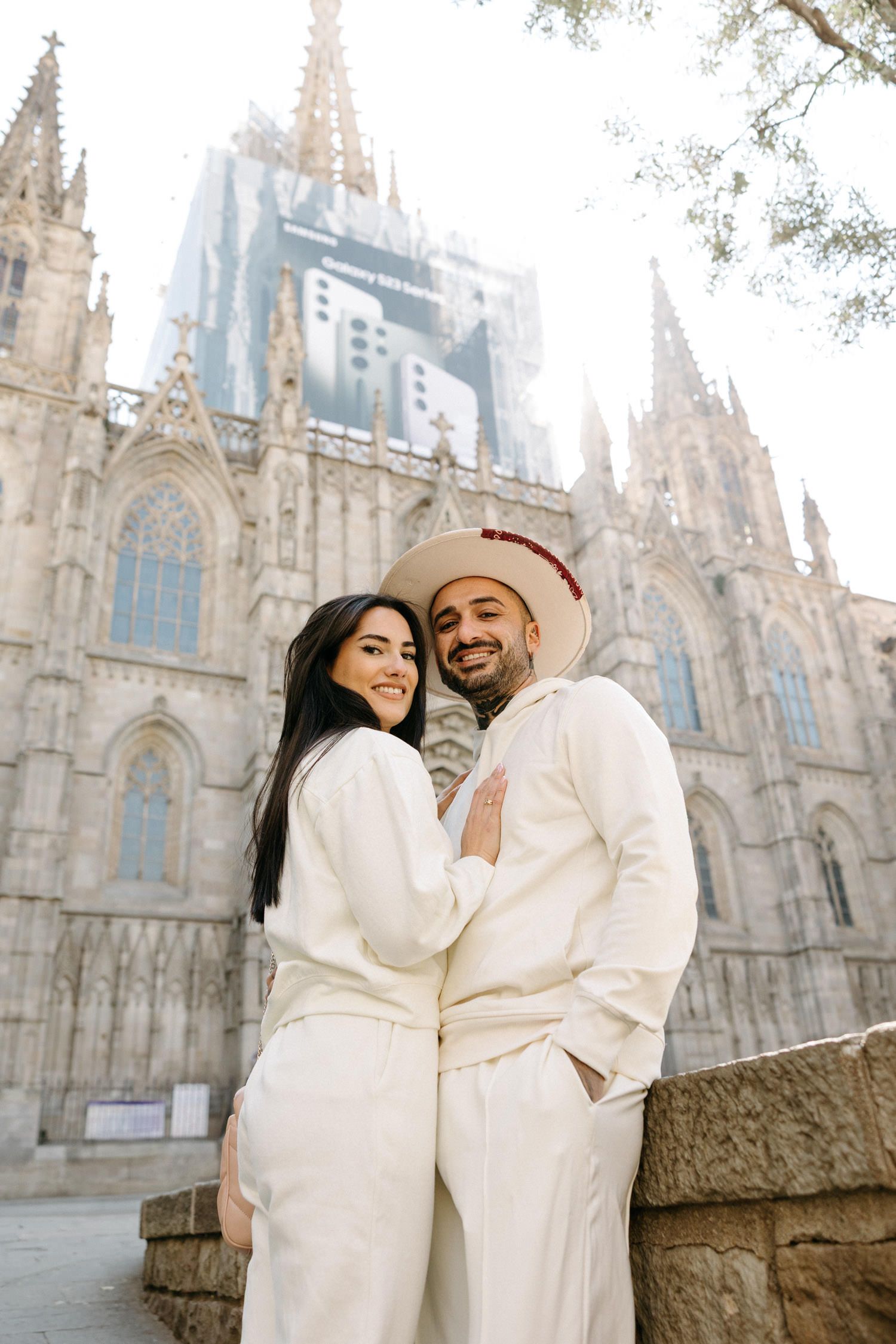 Couple in white outfits posing in front of the cathedral of Barcelona in the gothic quarter.