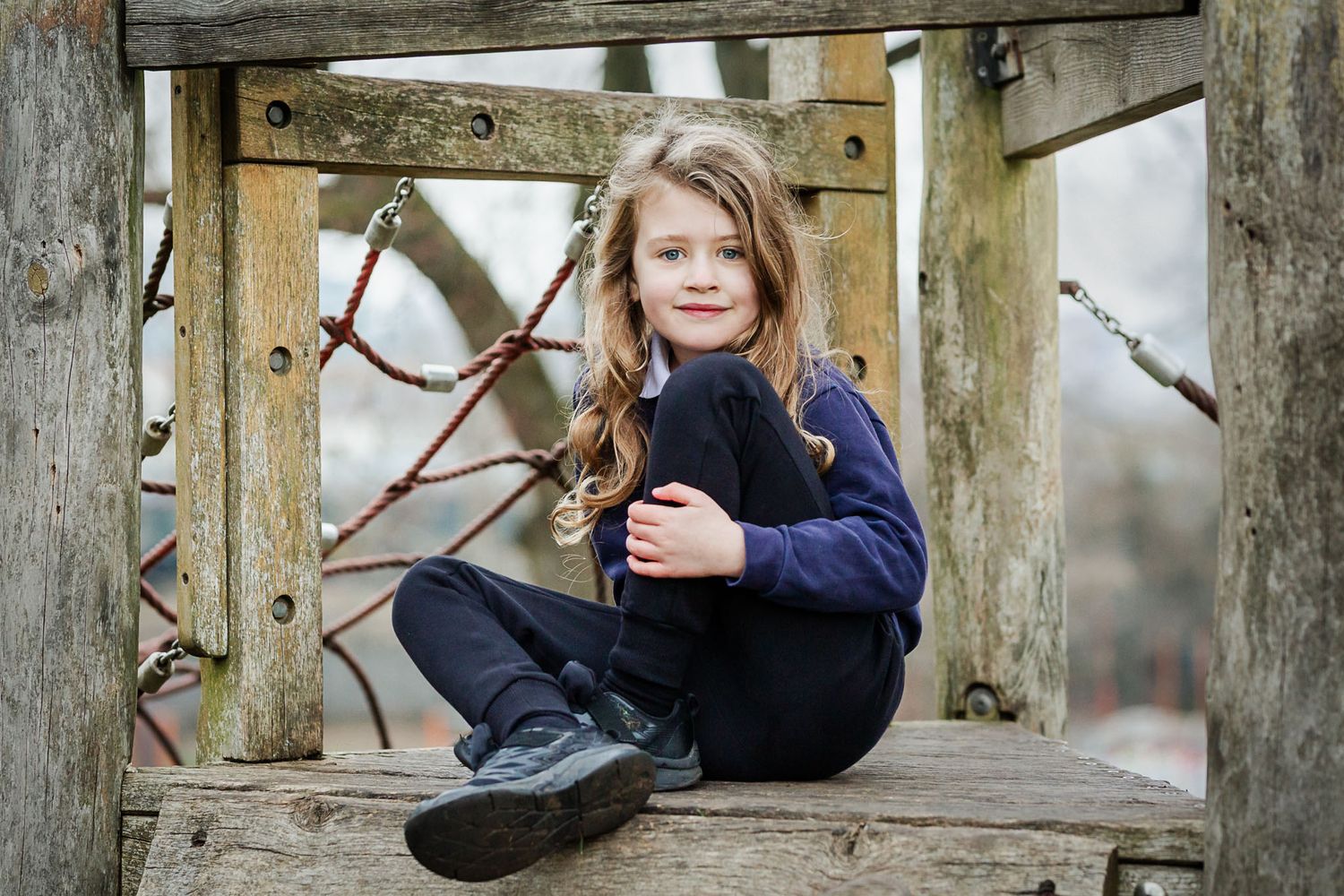 A school boy smiles naturally as he looks to camera whilst sitting on play equipment at a school photoshoot. Bristol school photography