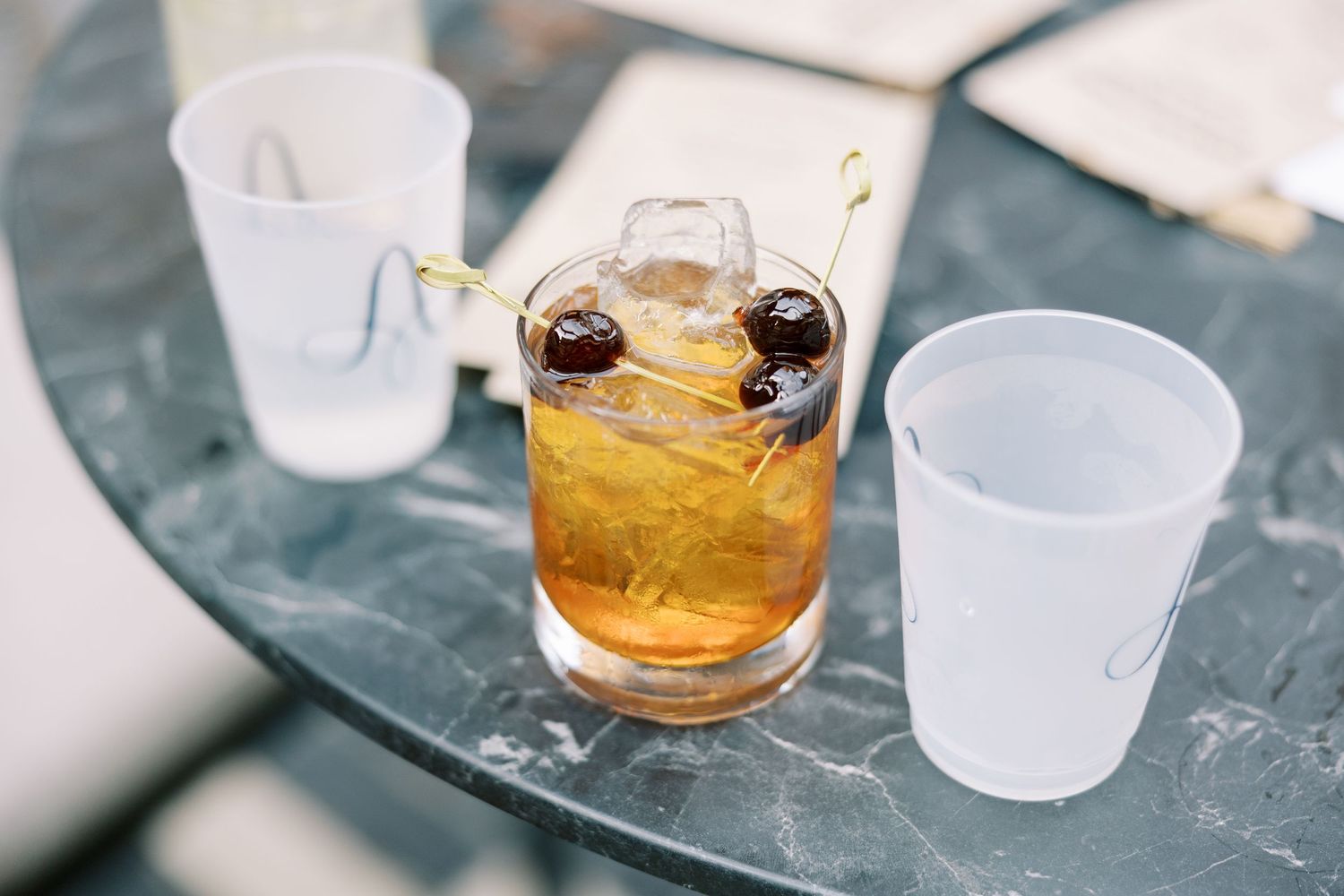 Cold clear ice cubes clink in a lowball glass with golden whiskey on a dark surface.