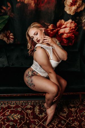 Boudoir photoshoot on dark velvet couch with red floral backdrop and vintage rug. Boudoir Photo Studio Michigan