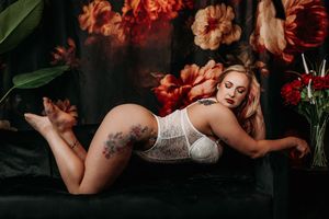 Artistic boudoir photo with white lace lingerie against dark backdrop with vibrant red florals and greenery.  Boudoir Photo Studio Michigan