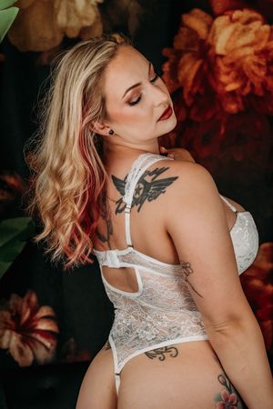 Close up portrait showing blonde hair with pink highlights and white lace lingerie against floral backdrop. Intimate Boudoir Photography
