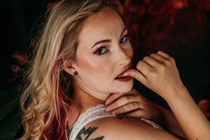 Artistic boudoir portrait featuring white lace lingerie and visible tattoos against a dark background with red lighting. Intimate Boudoir