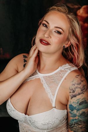 Glamour portrait in white lace bodysuit with visible tattoos and professional makeup styling. Intimate Boudoir Photographer Grand Rapids MI