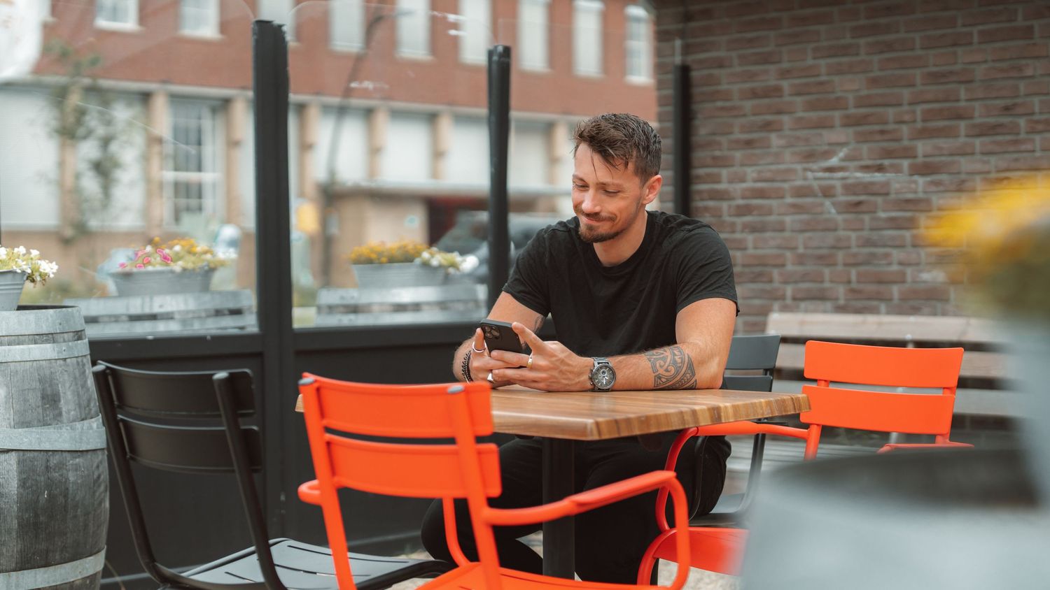 Person sitting at orange outdoor cafe table checking mobile phone in urban setting.