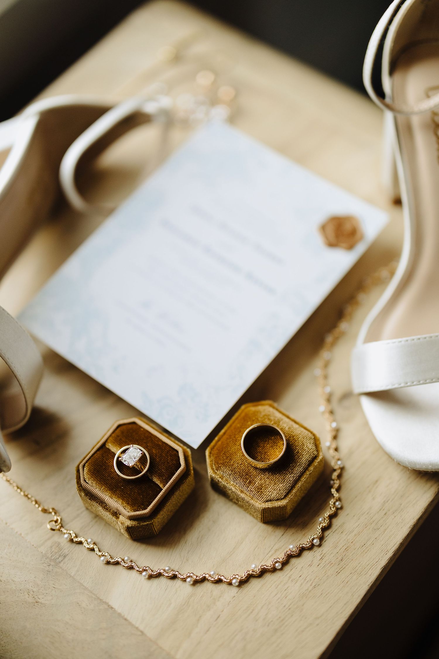 Wedding rings in brown velvet boxes next to invitation and white heels.