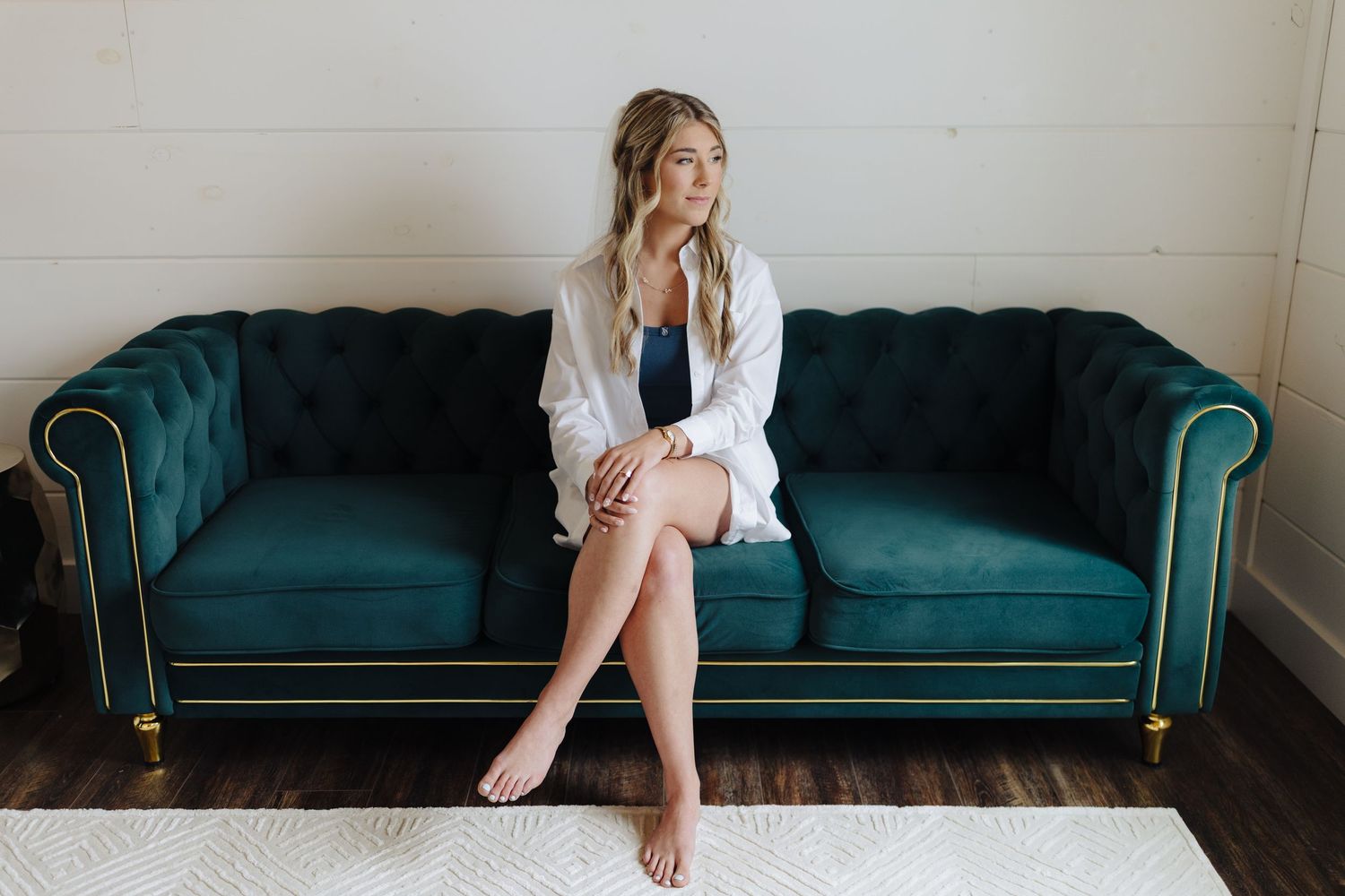 A person in a white blazer sits with crossed legs on a luxurious teal velvet Chesterfield sofa.
