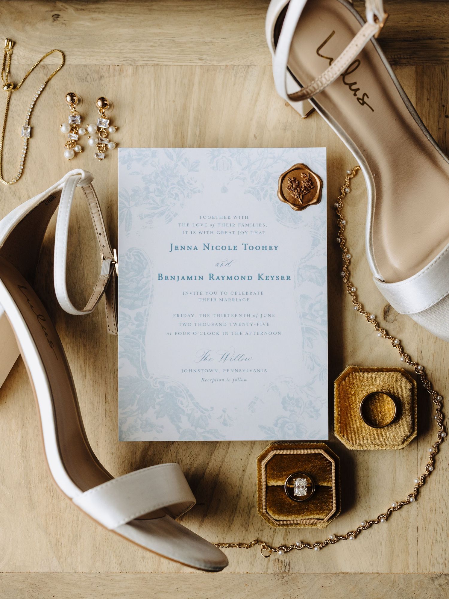 Wedding detail flatlay with elegant white shoes, invitations, jewelry and rings on a neutral background.