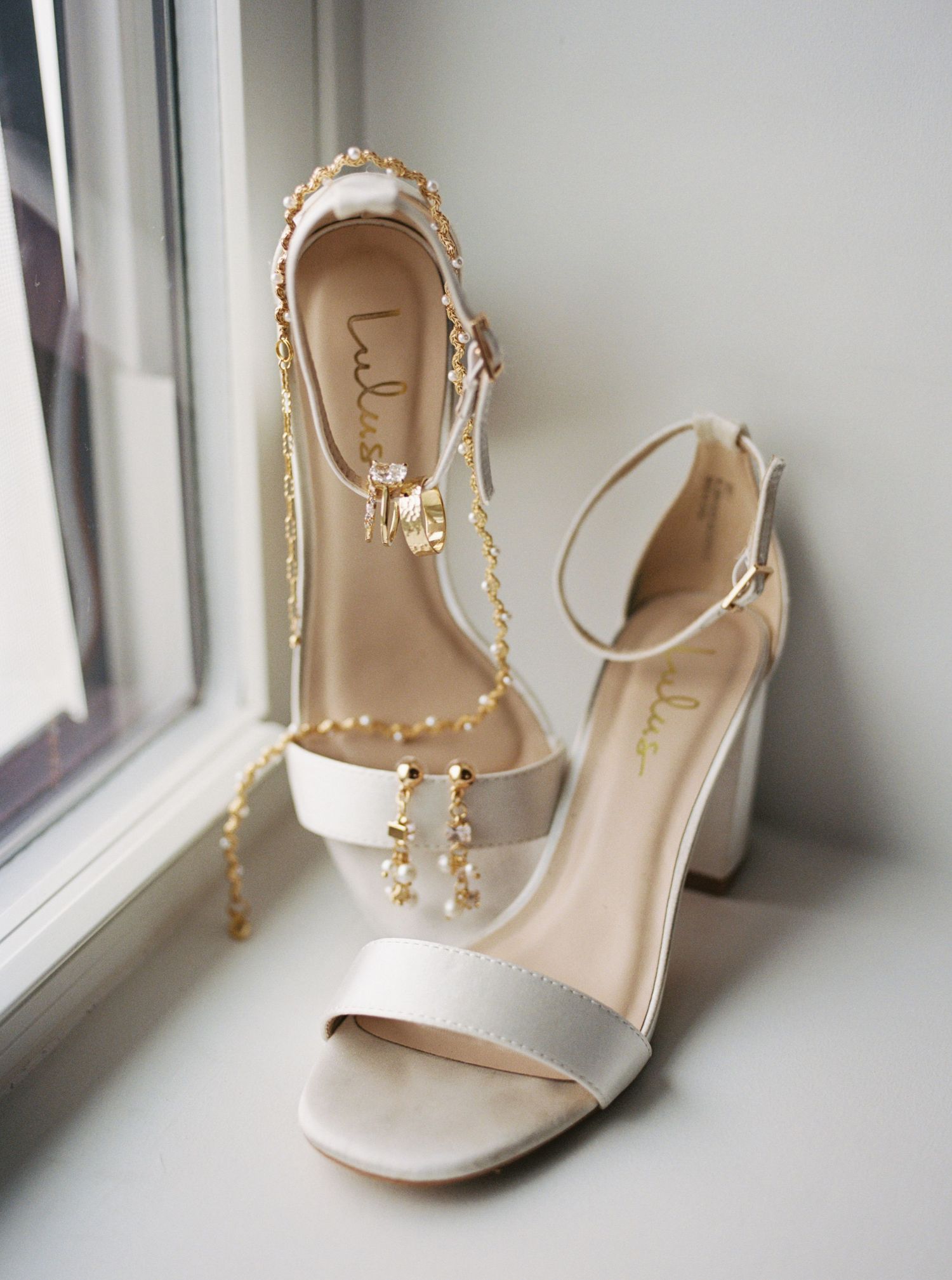 Elegant white wedding heels with pearl straps displayed on a windowsill.