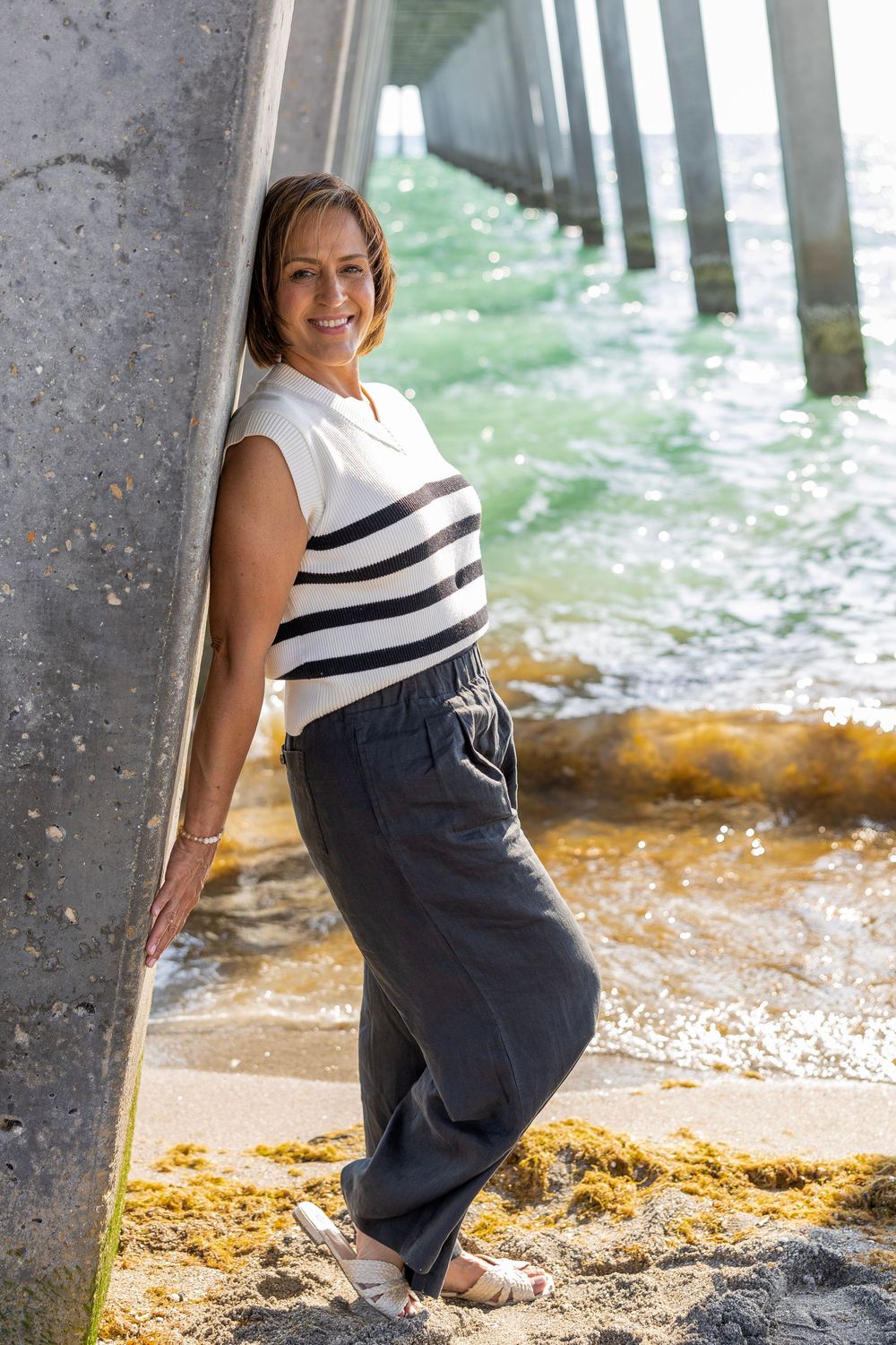 Woman in striped top leaning against pier column by ocean.