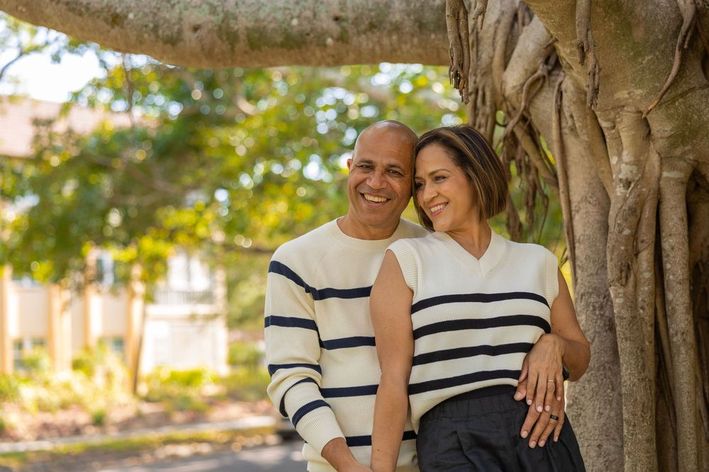 Happy couple in matching striped sweaters posing by tree.