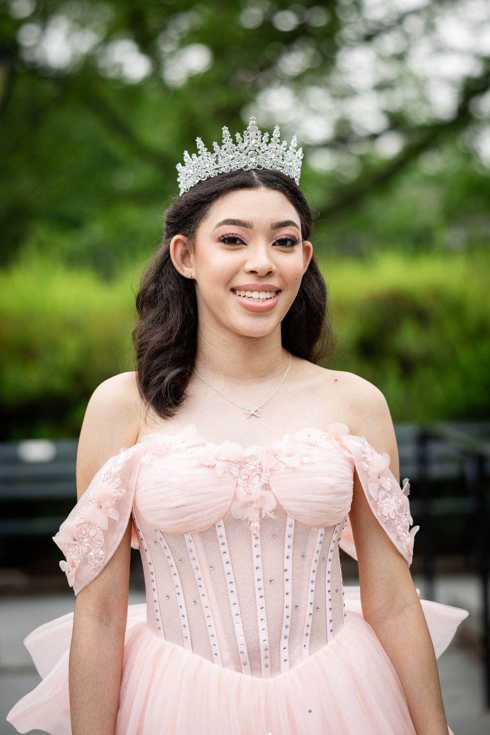 A person in a pale pink princess gown and tiara poses in an outdoor setting.