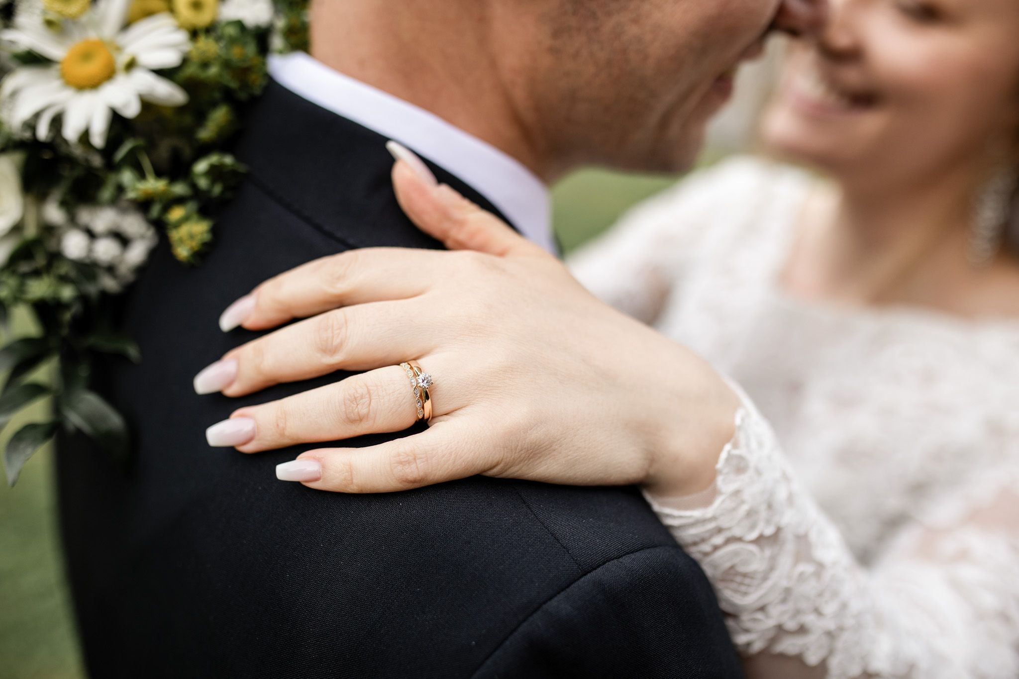 Detaljbild av ringen och brudpar i bakgrunden