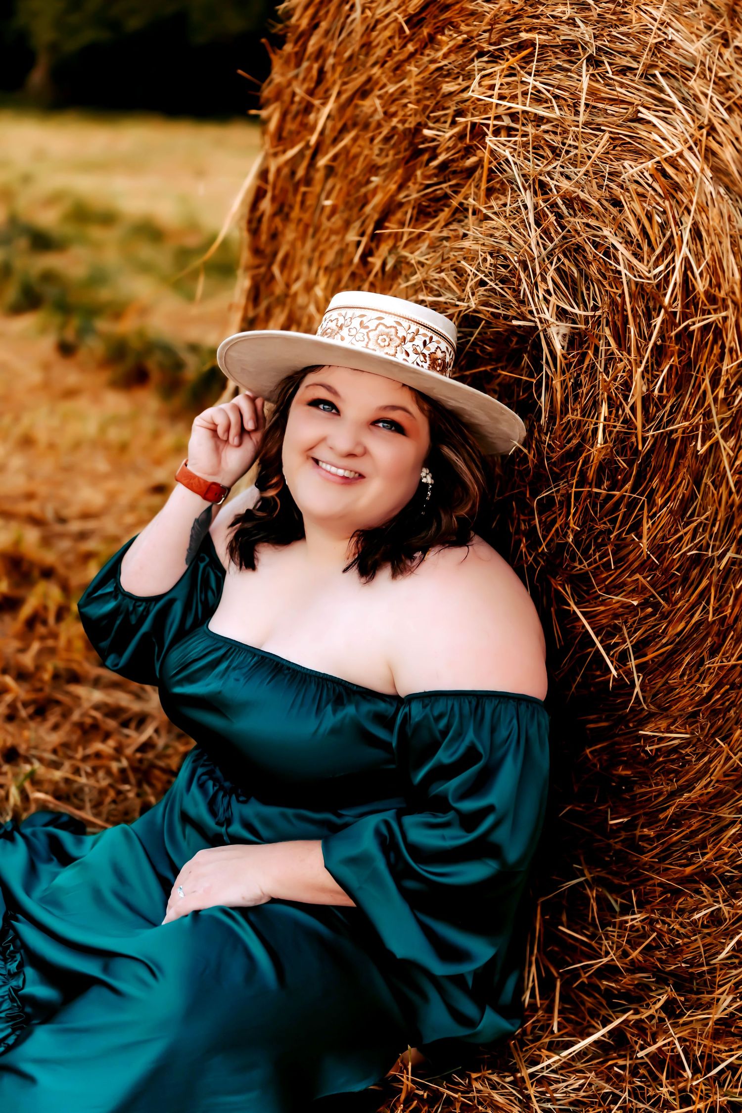 A person in a flowing teal dress stands in a golden autumn field at sunset with mountains silhouetted in the background.