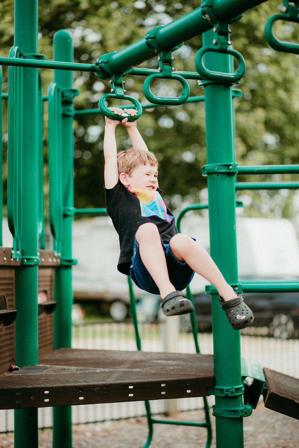 Child playing on green playground equipment outdoors at a local park.