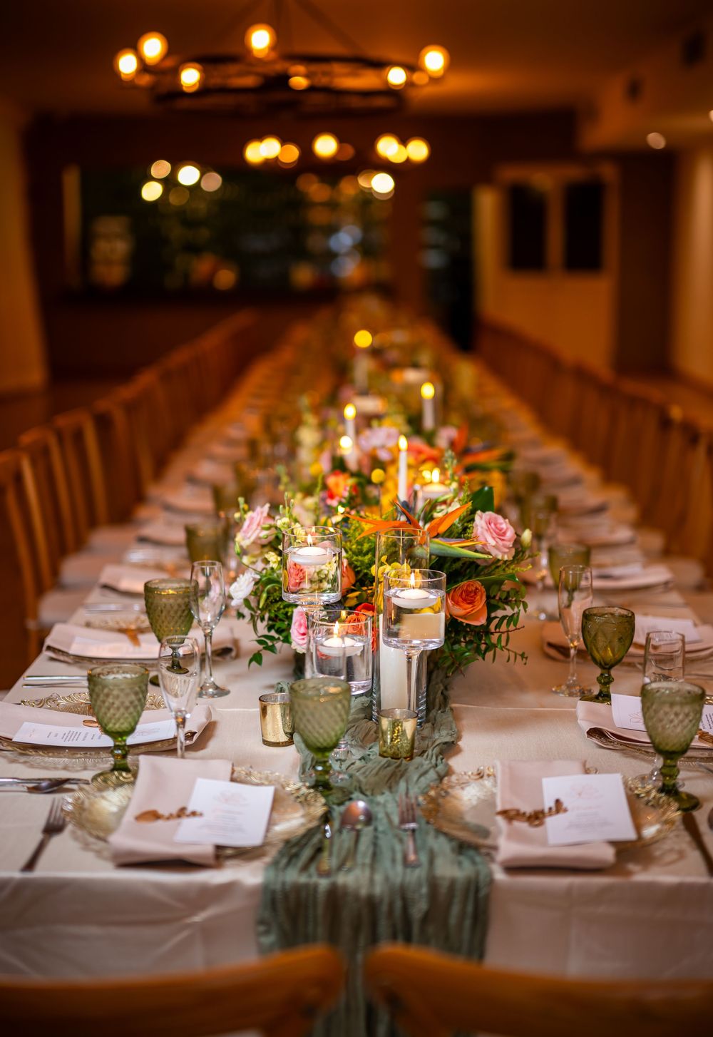 Elegant wedding reception table setting with candlelit centerpieces, green glassware, and romantic floral arrangements.