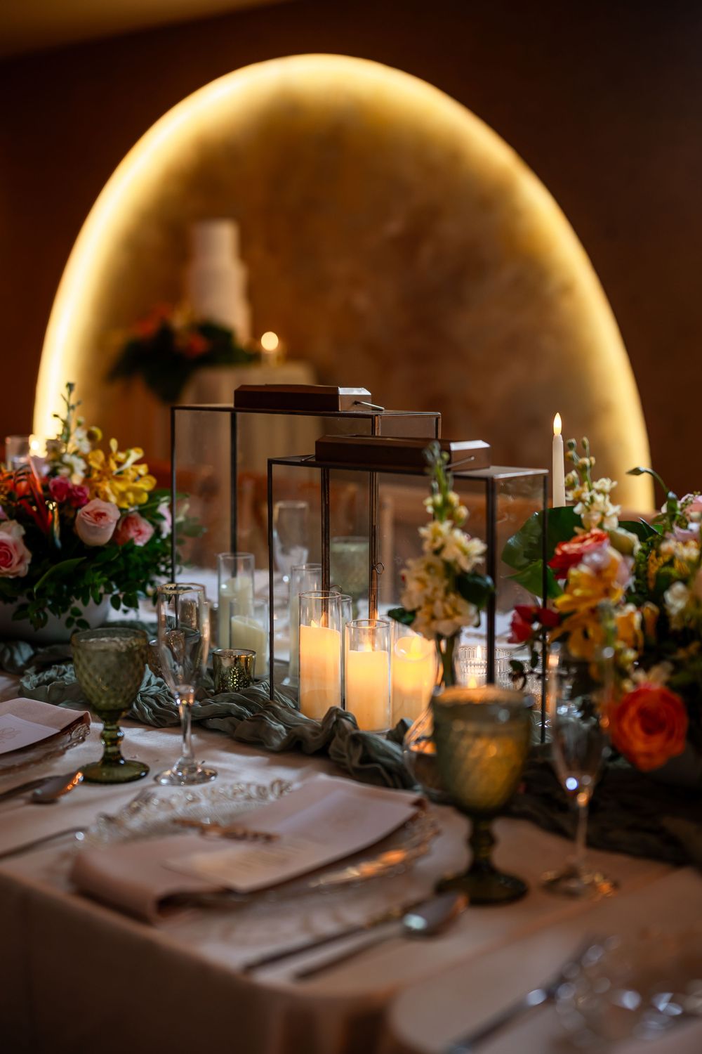Romantic table setting with lantern centerpieces and floral arrangements under warm arch lighting.