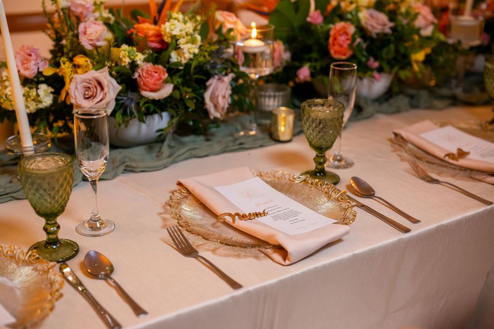 Wedding table place setting with green goblet, white napkin, and pink floral centerpiece arrangements.