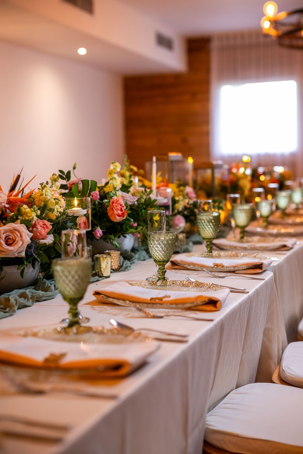 Elegant table setting with green goblets, coral flowers, and white linens at a wedding reception.