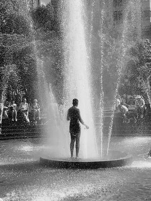 Silhouette of a boy standing in the middle of a fountain, water rising around him