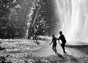 Dark silhouettes of two children running in a fountain with water splashing around