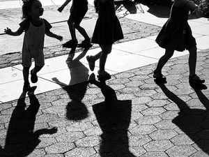 Black and white photo capturing the shadows of many children running on the ground