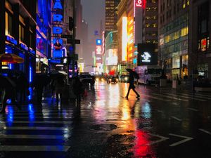 A man crossing the street in Times Square at night in the rain, with city lights reflecting on the wet pavement