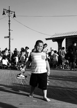 A child at Coney Island holding his sneakers, standing on the boardwalk