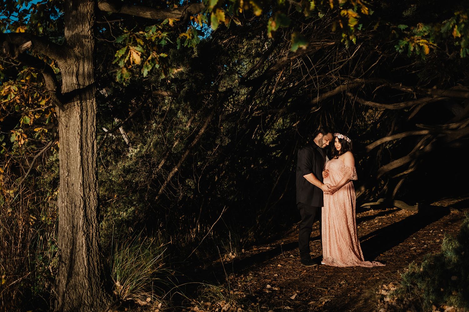Romantic maternity photoshoot in a wooded setting during golden hour.