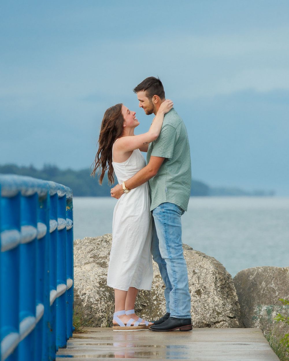 A tender embrace shared on a lakeside pier with blue railings against a serene water backdrop.