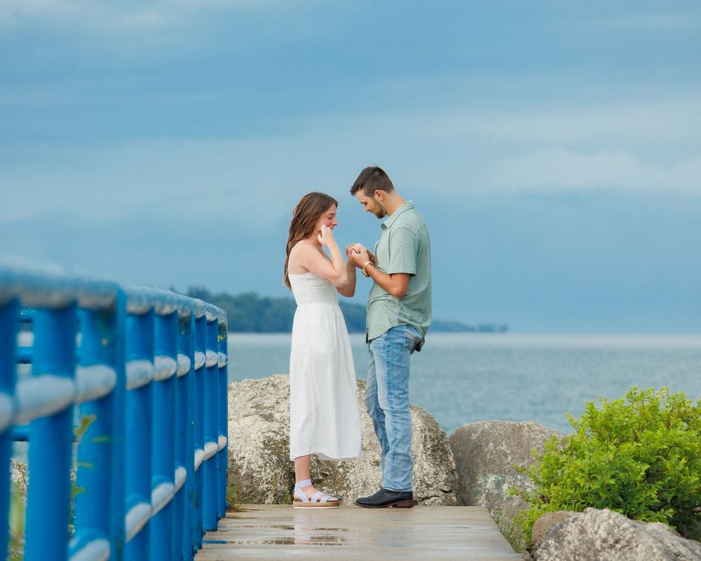 A couple shares a romantic moment on a pier with blue railings overlooking a serene ocean landscape.