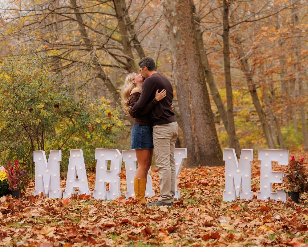 A romantic autumn engagement photo series showing a couple among fallen leaves in a wooded park setting.