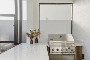 Modern outdoor kitchen area with stainless steel grill and wooden accents under a covered patio.