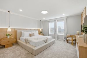 Modern bedroom interior with white bedding, beige carpet, and natural light streaming through large windows.