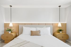 Bright and minimalist bedroom design with white bedding, wooden accents, and pendant lighting creates a serene atmosphere.