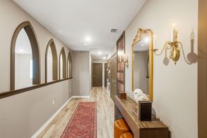 Long hallway with arched doorways features elegant wood trim and a traditional red runner carpet leading the way.