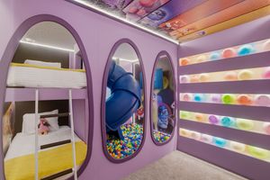 A colorful indoor play area with purple walls, circular windows, and rainbow-colored lighting effects.